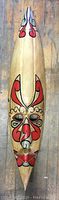 Front view of a tall, elongated wooden mask with painted red, black and white designs.