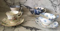 Four vintage tea cups and their matching saucers arranged on a marble surface, showcasing different floral and classic blue and white designs.