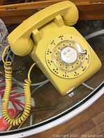 Front angled view showing rotary dial, handset, and coiled cord on glass surface.