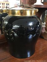 Front and side view of large black glossy ginger jar showing rounded ceramic body and brass fittings.