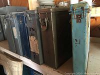 Front view of six metal film reel cases in blue and grey colors, lined up on a shelf showing wear and labels.