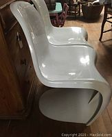 Side view of two white molded plastic Panton chairs placed side by side, highlighting their seamless S-shape design and glossy finish.