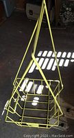 Yellow metal wire tennis ball hopper basket with handle, viewed from side angles showing structure