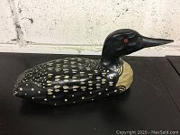 Full side view of the wooden loon decoy showing the black body with white spots and beige neck.