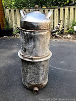 Full view of the metal still showing its cylindrical shape and handles.