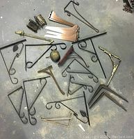 Full view of lot showing various metal brackets, springs, a decorative knob, and metal braces laid out on a concrete floor.
