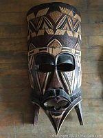 Front view of large wooden mask showing geometric carved patterns and flat top.