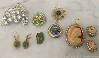 Jewelry lot arranged on white marble surface, showing all pieces including cameo pendant set, brooches, and earrings