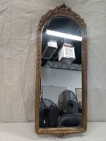 Full front view of the narrow arch mirror with ornate gold-colored frame in upright position.