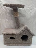 Front view of grey cat tower showing house-like base with cubby hole and window, vertical pole partially wrapped with sisal scratching rope, and top perch platform.