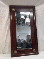 Cherrywood framed hanging mirror leaning against a wall showing clear reflection and decorative brass corners.