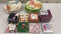 Photo of various stacks of decorative paper plates and multiple stacks of napkins with different colorful printed themes showing humor and celebration motifs.