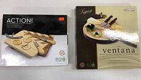 Two boxed cutting board sets: 'Action!' and 'Ventana' by Legacy displayed side by side.