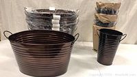 Lot of 12 garden planters showing brown oval metal tubs and smaller black metal pots, all new.