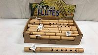 Box containing 23 new bamboo flutes with natural finish and display header.