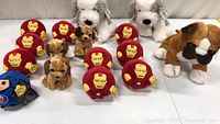 Lot of 16 stuffed plush animals arranged on a white surface including multiple Iron Man heads, white dogs, brown dogs, and a bulldog.
