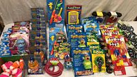 View of multiple new kids toys including stretched figurines, eye popper toys, fuzzy face character, splash and bubble machines, bracelets, and fishing game