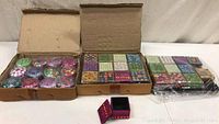 Boxes in open cardboard boxes showing sets of small, colorful, decorated jewelry boxes in rows with assorted bright colors and patterns.