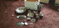Photo showing the complete set of silver plated dishware and utensils including trays, serving pieces, and candlestick holders arranged on carpeted floor