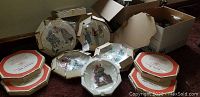 Six Norman Rockwell collector plates, still boxed and wrapped in original plastic coverings, arranged on floor with visible artwork and box tops.