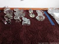 Photo of clear glass animal figurines including pigs and ducks, candy dish, and other items on a brown surface.