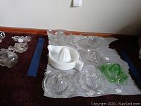 Overview of seven citrus juicers, mostly glass, arranged on a surface with some smaller glass items to side.