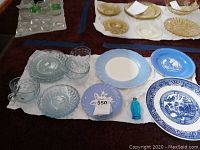 Set of various ceramic plates and clear glassware arranged on cloth with price tag visible