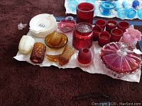 Multiple glass items displayed on a towel: amber and cranberry candle holders, candy dishes, dessert plates, and glass boot.