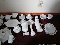 Overview of milk glass condiment servers, candy dishes, sugar bowls, butter dishes, and candle holders spread on floor.