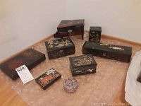 Eight black lacquer boxes including five jewelry boxes with various hand-painted Asian floral designs, one black lacquer tissue box, one black lacquer glove box, and one round fabric trinket box on bubble wrap.
