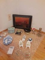 Full view of the lot items including Asian photo album, brass candle holder, brass ceramic rose, ceramic pin holders, blue tin box, black ceramic bowl, two framed wall art pieces, and small decorative items.