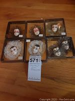 Overview of all seven boxed Glamour Girl brooches arranged on wooden floor, showing different face designs and materials.