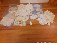 Wide shot showing assortment of crocheted and cross stitched doilies laid out on the floor