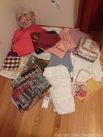 Wide view of multiple folded linens including tablecloths, runners, and placemats in various colors and patterns placed on a flat surface.