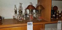 Shelf display of multiple kerosene lamps showing rounded bases and metal shades