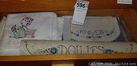 Drawer containing folded embroidered linen pieces with kitten designs, labels including 'Knives' and rolled 'Doilies'.