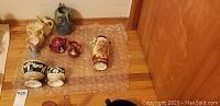 Overview photo showing all ceramic pitchers, sugar dishes, and vases arranged on bubble wrap on a wood floor.