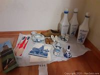 Photo showing the full collection of items: three tall liquor bottles, wooden shoes, girl figurine, bell, three hand-painted ceramic cups, salad utensils in box, and three Delft plaques.