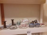 Photo shows teapot, cup, saucer, shot glasses, brass candle holders on ceramic plates, and decorative plates on shelf.