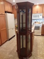 Full view of the tall wood and glass display cabinet showing hexagonal base and glass panels