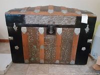 Front view of the trunk showing wood slats, textured metal panels, black trim, and lock on front center.