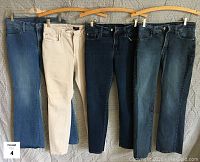 Four pairs of women's jeans hanging on wooden hangers, medium blue denim, cream, dark blue denim, and light blue denim.