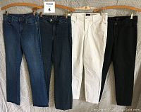 Four pairs of pants hanging on hangers including two blue denim jeans, one white, and one black pants.