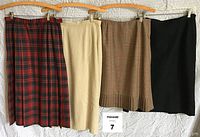 Four skirts hung on hangers: red plaid Pendleton (size 12), tan linen (size 10), brown plaid Pendleton with pleated hem (size 8), black wool skirt (fits like size 10), shown front view.