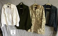 Front view of all four items: white DKNY jacket, green poncho, floral raincoat, blue denim jacket.