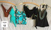 Five bathing suit pieces hanging on wooden hangers on beige fabric background: brown bikini top, turquoise padded bikini top, turquoise floral tankini top, black bikini bottom with turquoise detail, brown bikini bottom.