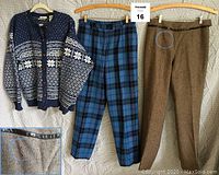 Front view of sweater and two slacks hanging on hangers, showing Nordic sweater in blue and white, plaid pants, and tweed pants with leather trim and holes circled.
