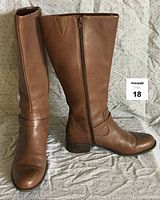 Front-side view of the brown leather boots showing side zipper and decorative strap detail with heel.