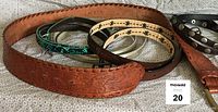 Five leather belts arranged together including a brown embossed Ralph Lauren belt, a silver leather-like belt, and a turquoise snake skin dyed leather belt showing wear.