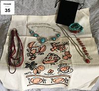 Overview of all items laid out on embroidered kitchen towel: multi-strand beaded necklace, turquoise stone silver-tone necklace, turquoise and coral bracelet, coral stone necklace and matching bracelet, vintage embroidered kitchen towel, small black velvet bag.